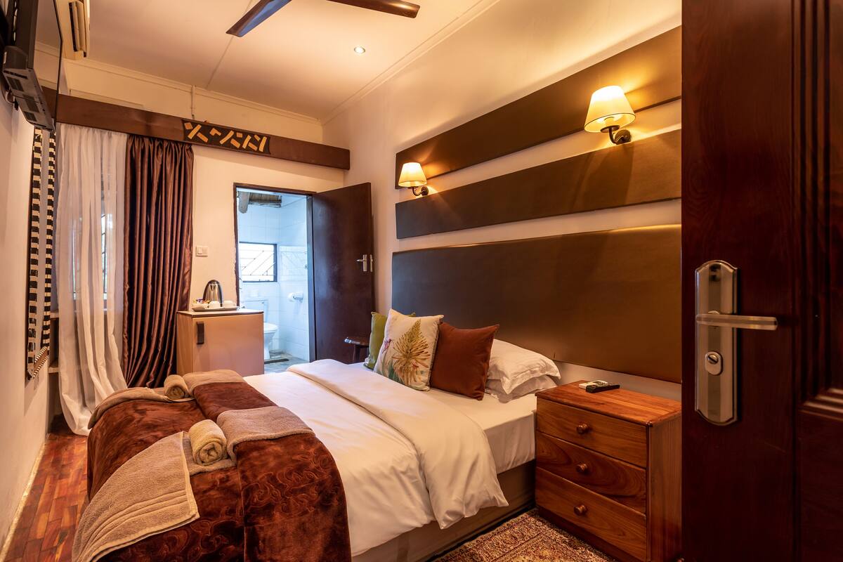 Een hotelkamer met een groot bed, nachtlampjes, een houten nachtkastje en een deur met een handgreep.