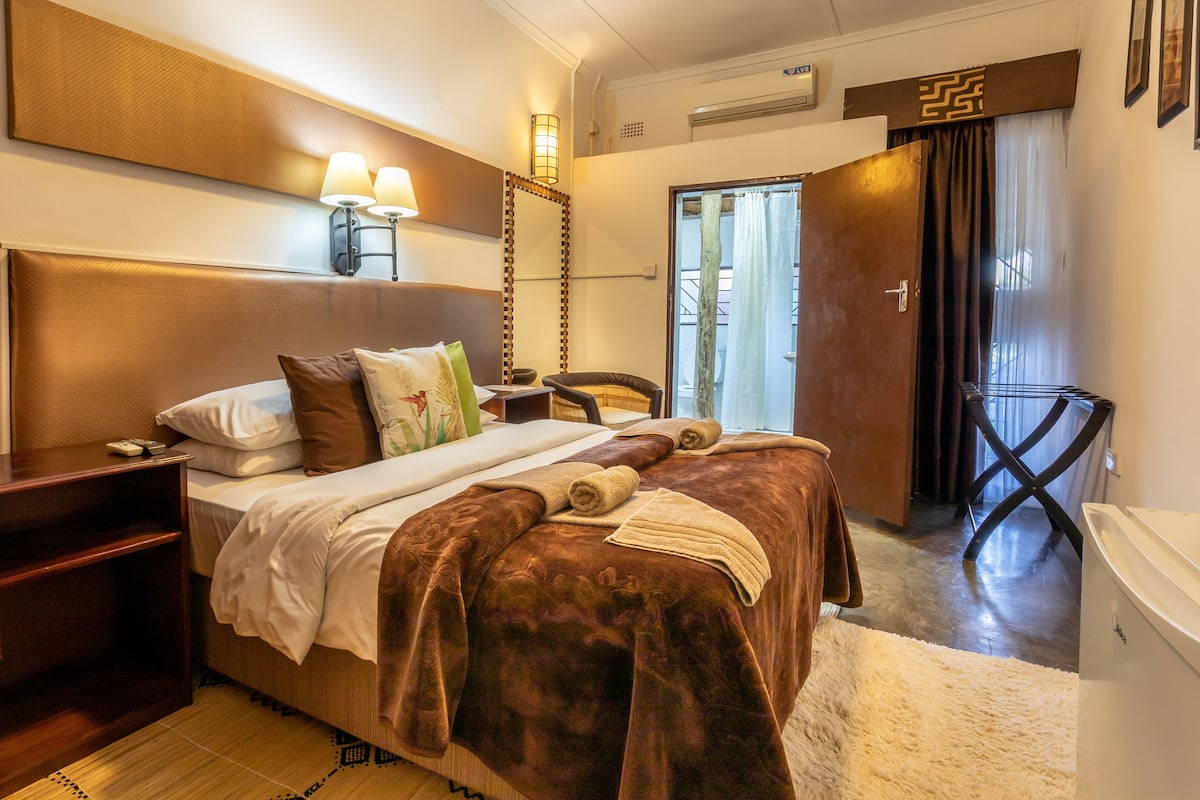 Een hotelkamer met een groot bed, bedlampen, een houten hoofdbord, een klein tafeltje en een stoel.
