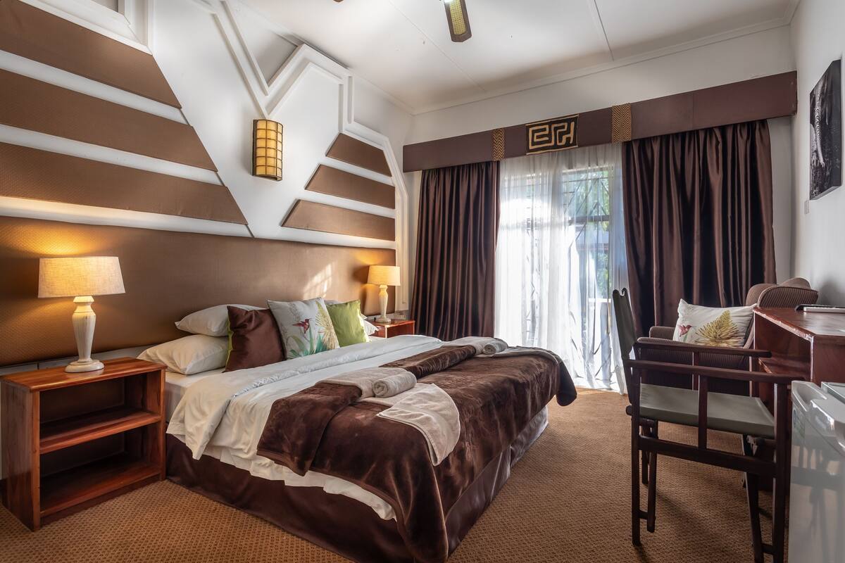 Een hotelkamer met een groot bed, twee nachtkastjes met lampen, een bureau met stoel, en uitzicht op het omliggende landschap door het raam.