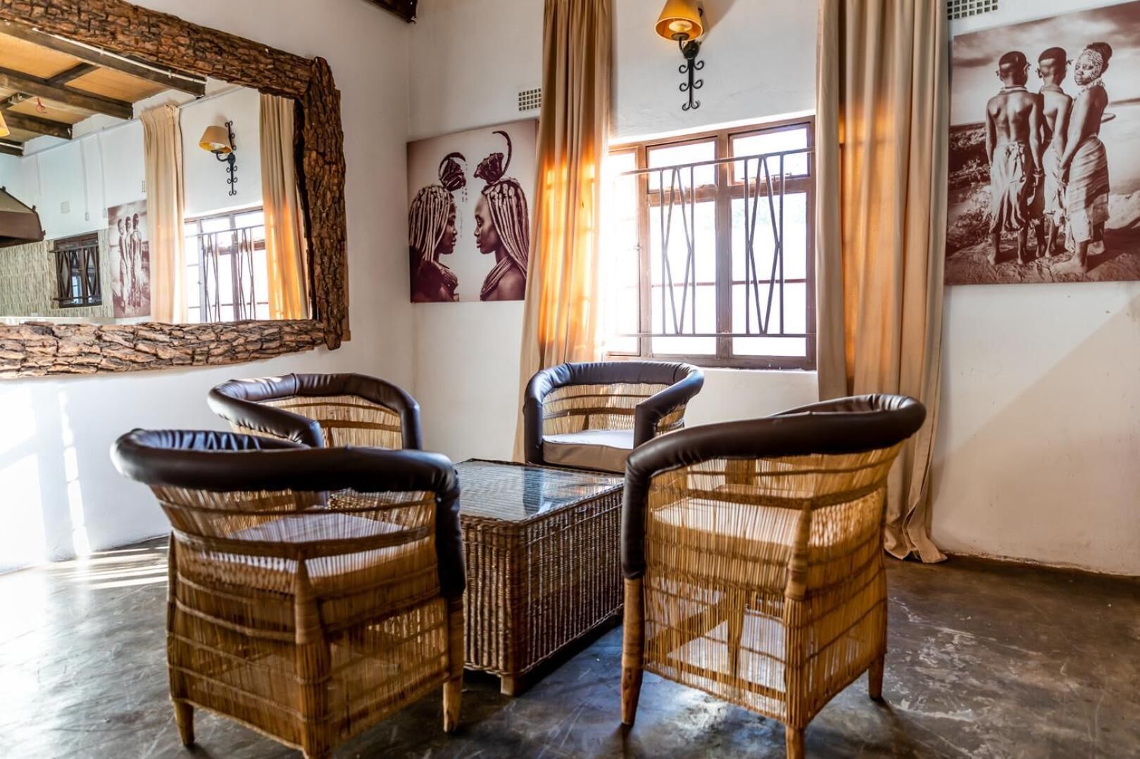 Un comedor con sillas de mimbre, una mesa de vidrio, un espejo grande y obras de arte en las paredes.