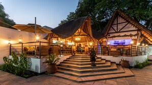 Un edificio rústico con techo de paja, una zona de bar y mesas al aire libre.