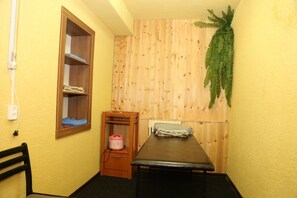 A small room with a wooden wall, a window with a shelf, a bed, a table, and a plant. - Hotel Dostuk (Bishkek)