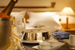 A neatly arranged hotel room with a bed, a bedside lamp, a bottle, glasses, and a tray with small items. - Hotel Dostuk (Bishkek)