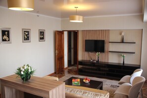 Una sala de estar moderna con una mesa de centro de madera, un sofá, un televisor montado en la pared y una pequeña planta sobre la mesa.