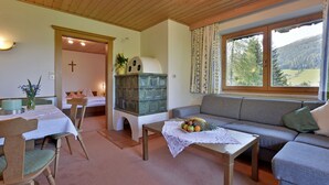 A cozy living room with a sofa, dining table, and chairs. There's a window with a view of trees and mountains. - Landhaus Alpbach (Alpbach)