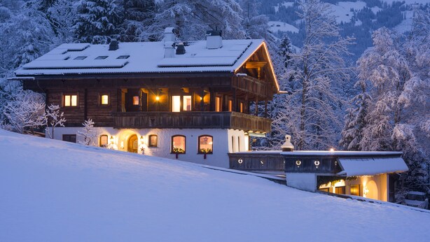 A wooden chalet with a balcony, surrounded by snow-covered trees and a mountain backdrop. - Landhaus Alpbach (Alpbach)