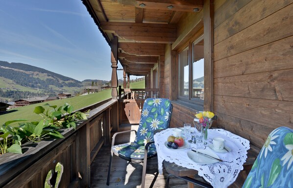 A wooden balcony with a table set for two, overlooking a mountainous landscape. - Landhaus Alpbach (Alpbach)