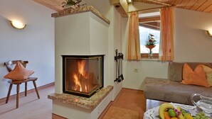 A cozy living room with a fireplace, a sofa, a dining table with fruit, and a chair. - Landhaus Alpbach (Alpbach)