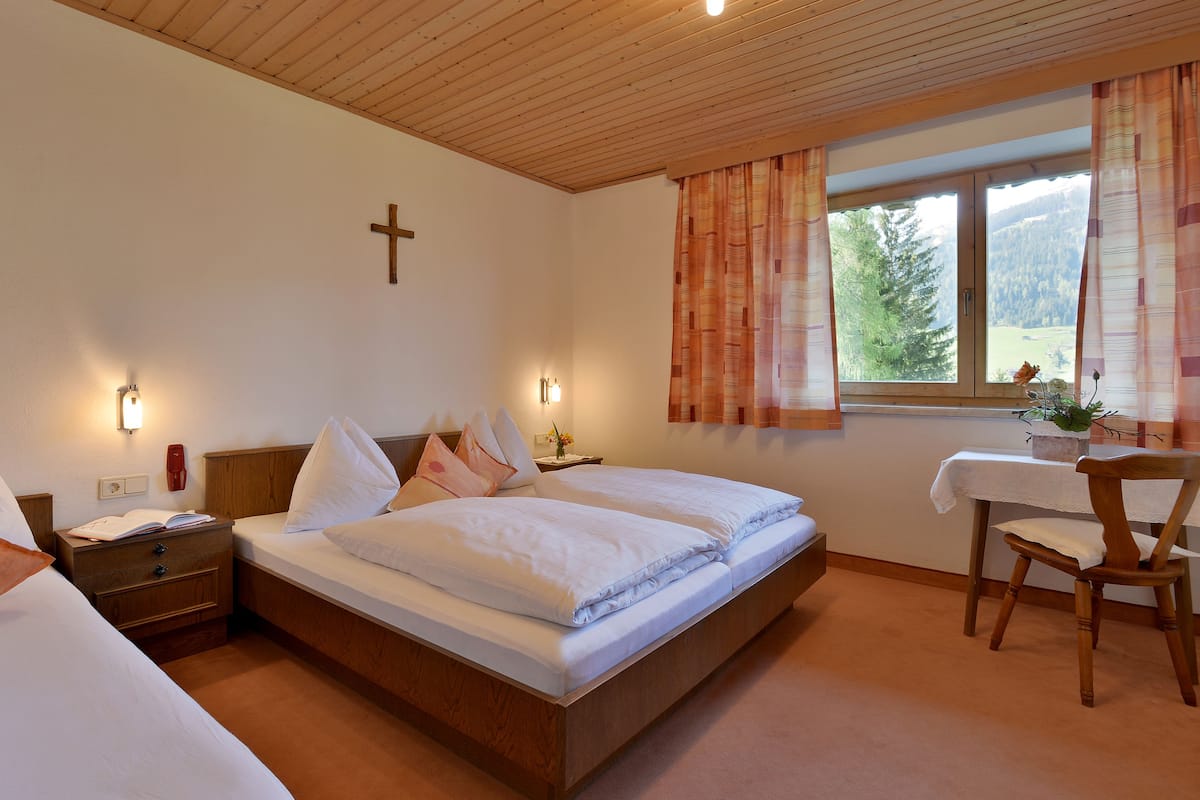 Un dormitorio con cama de madera, mesitas de noche, una cruz en la pared y una ventana con cortinas.