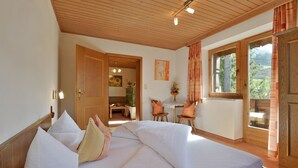 A bedroom with a wooden ceiling, a bed with white bedding, a wooden door, and a window with curtains. - Landhaus Alpbach (Alpbach)