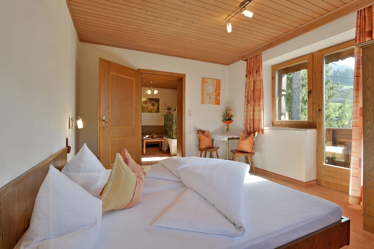 Un dormitorio con techo de madera, una cama con ropa de cama blanca, una puerta de madera y un ventanal con cortinas.