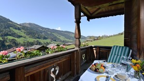 A wooden balcony with a table set for dining, overlooking a mountainous landscape. - Landhaus Alpbach (Alpbach)