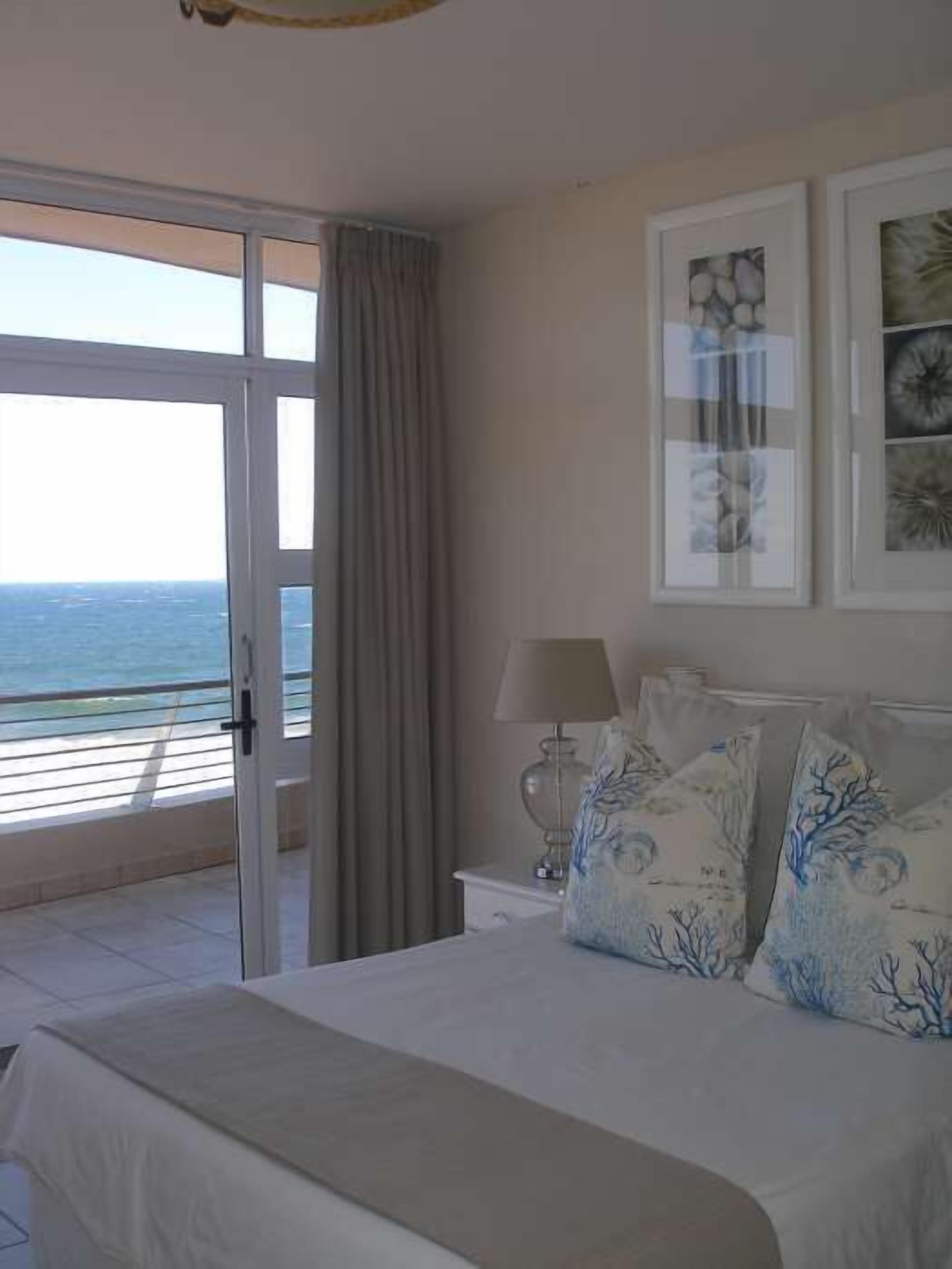 A bedroom with a bed, a nightstand, a lamp, and a view of the ocean through a sliding door.