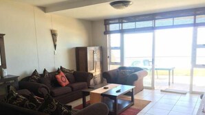 Una sala de estar con un sofá, una mesa de centro y un sillón. Hay un aparador y una ventana con persianas.
