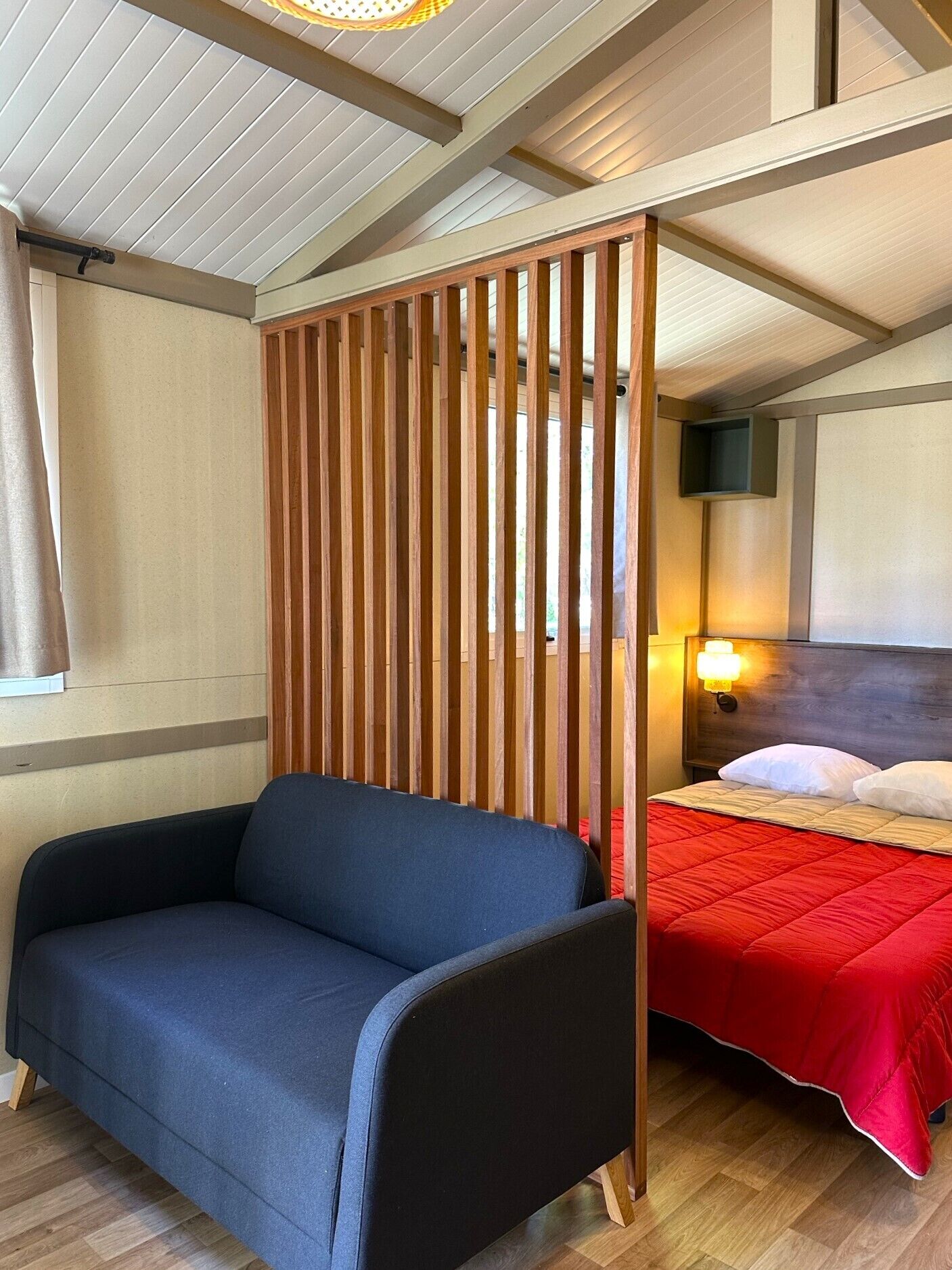 A room with a blue sofa, a bed with a red bedspread, and a wooden partition.