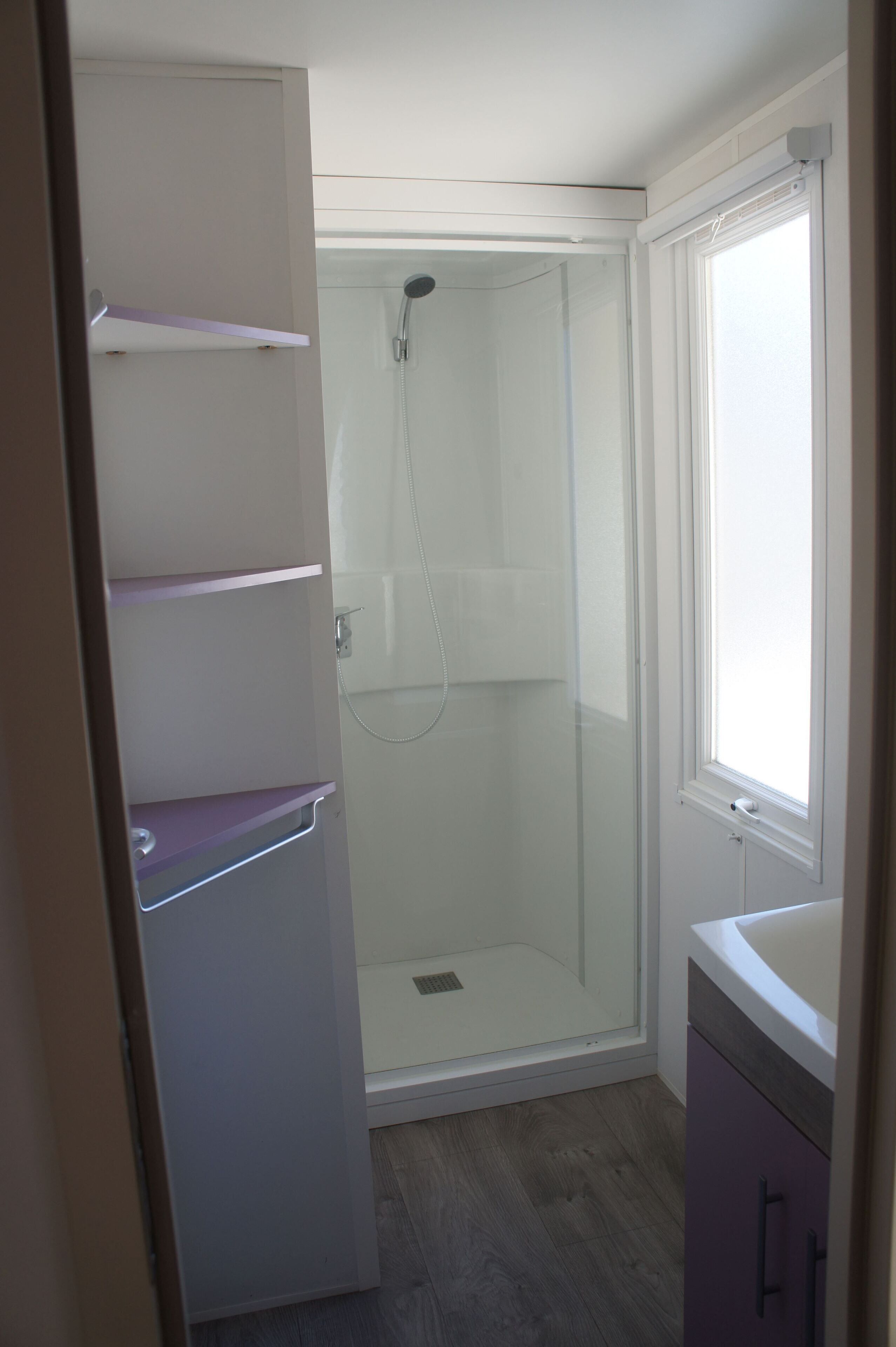 Een badkamer met een douchecabine van glas, een raam en een ingebouwde plankkast.