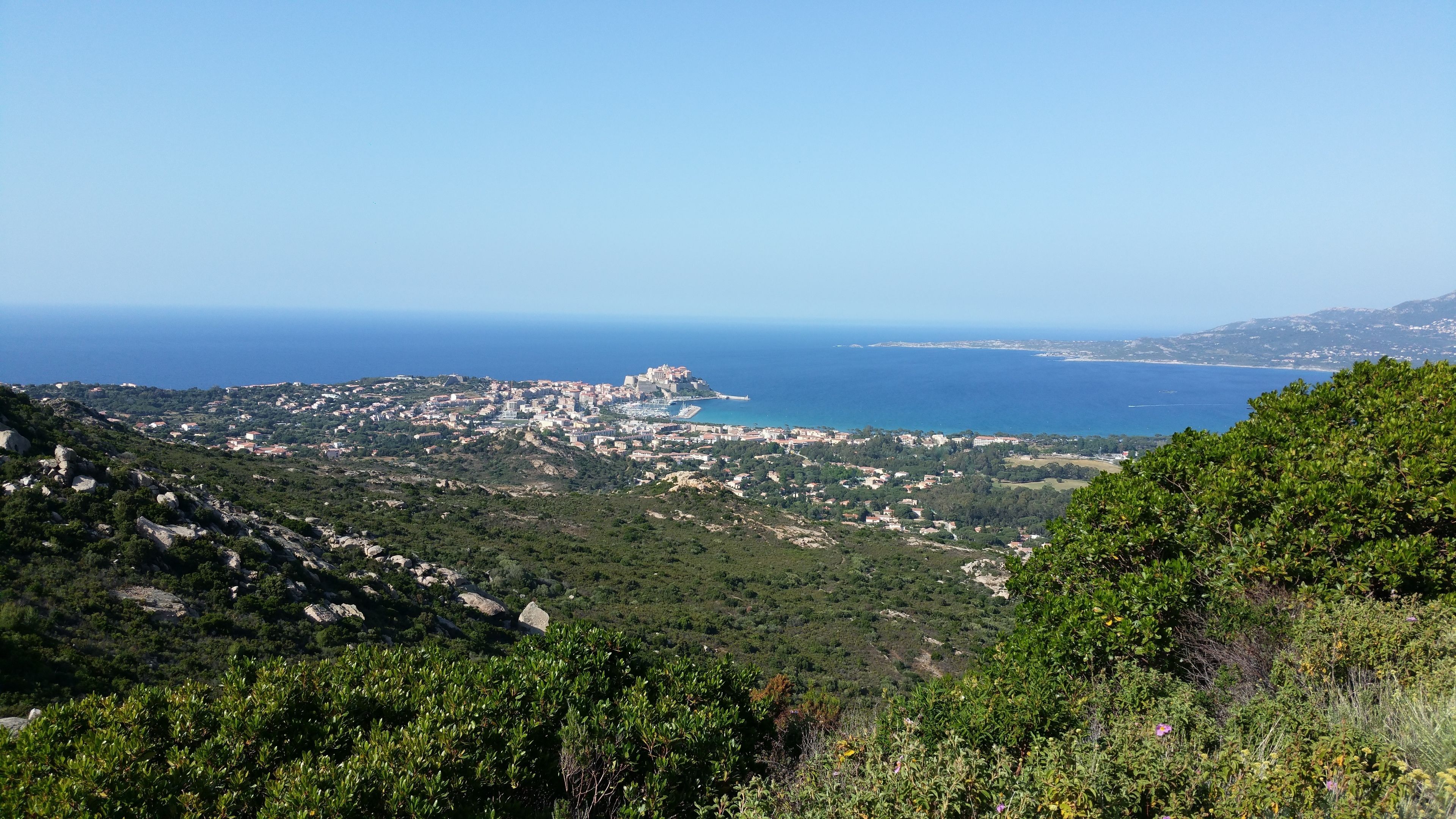 Eine Küstenstadt mit einer markanten Burg, die über das Meer blickt, umgeben von Grünflächen und felsigem Gelände.