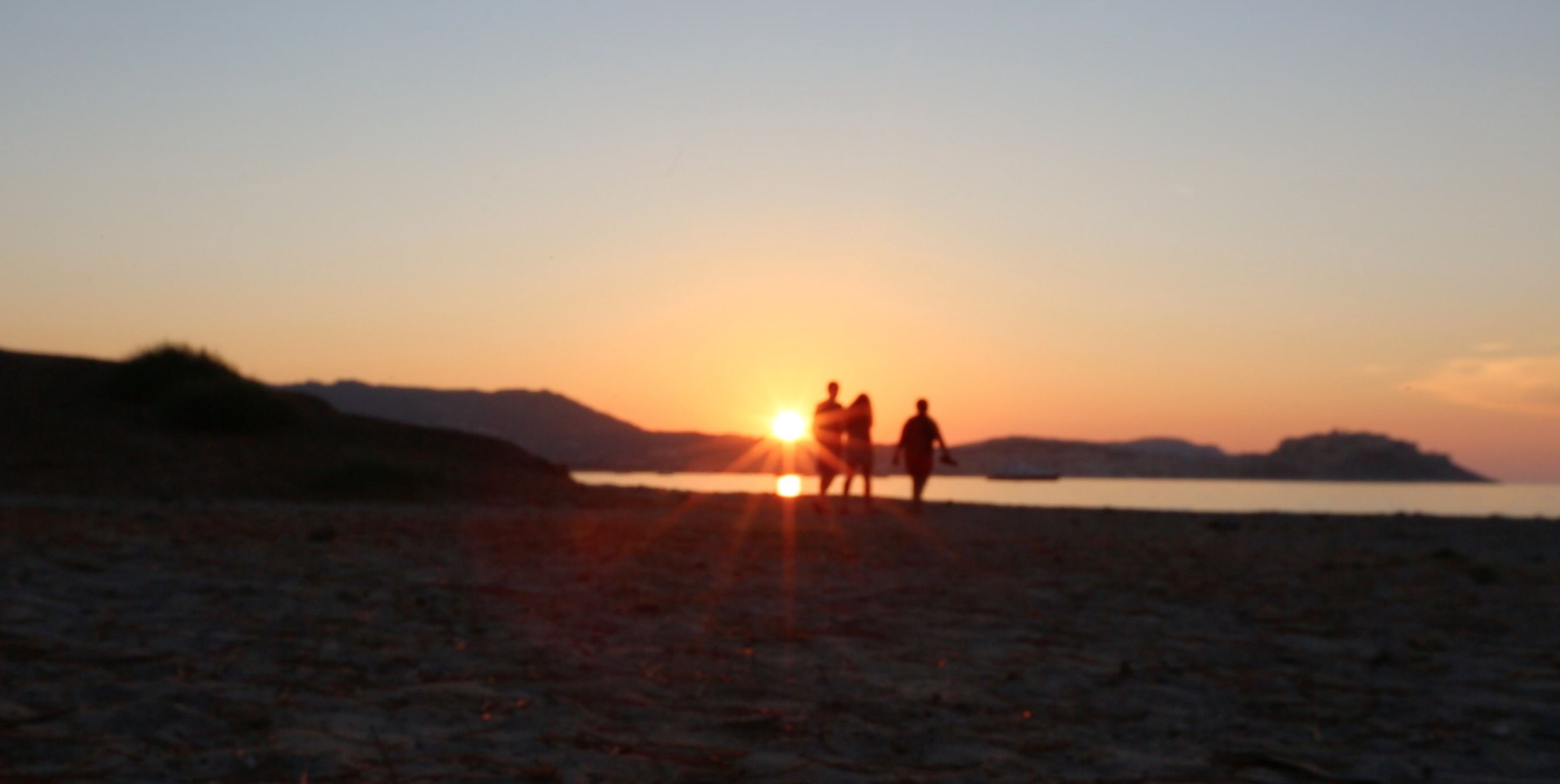 Un coucher de soleil sur une plage, avec les silhouettes de personnes et de chevaux.