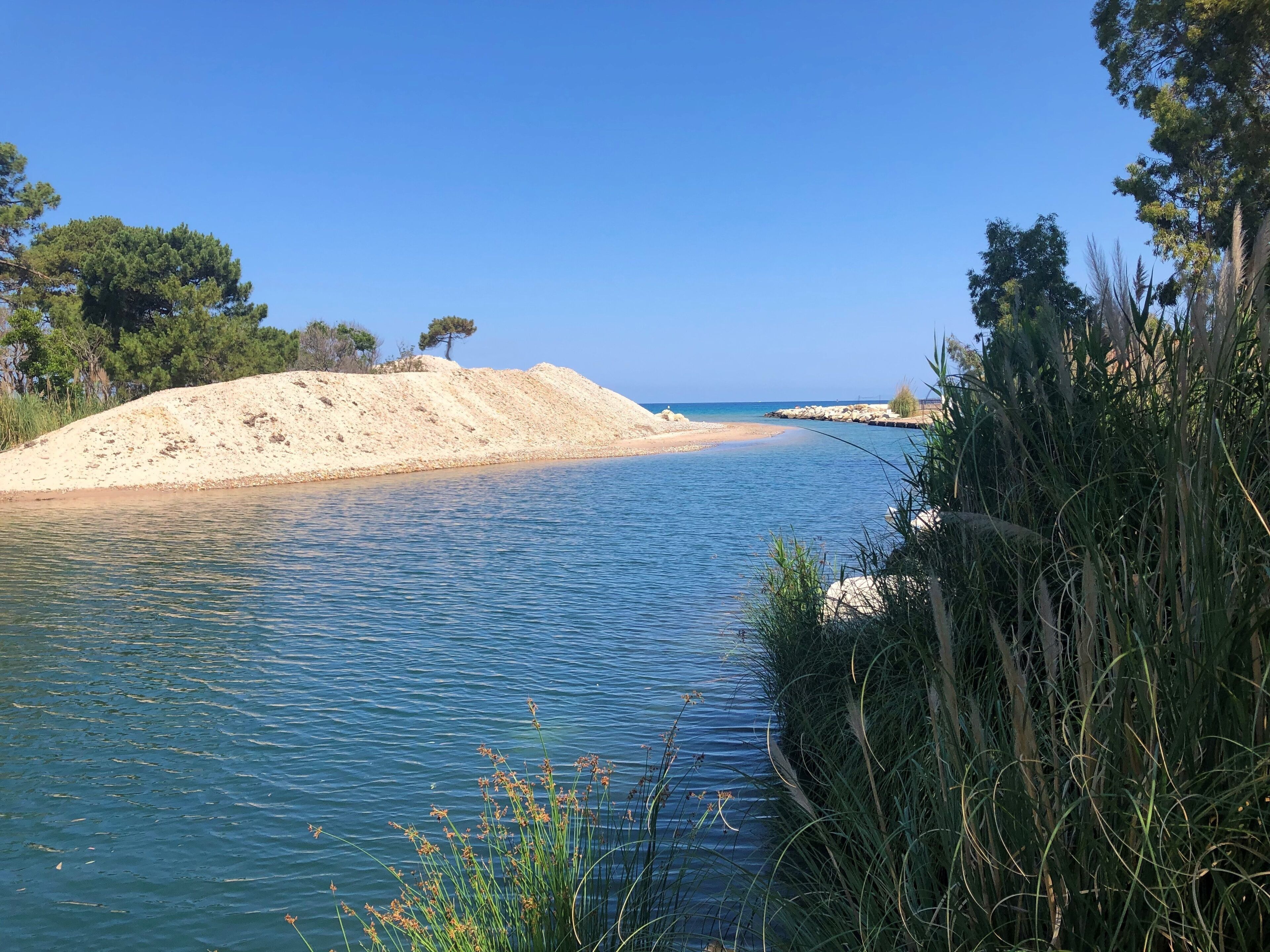 A coastal landscape with a sandy beach, clear blue water, and surrounding vegetation.