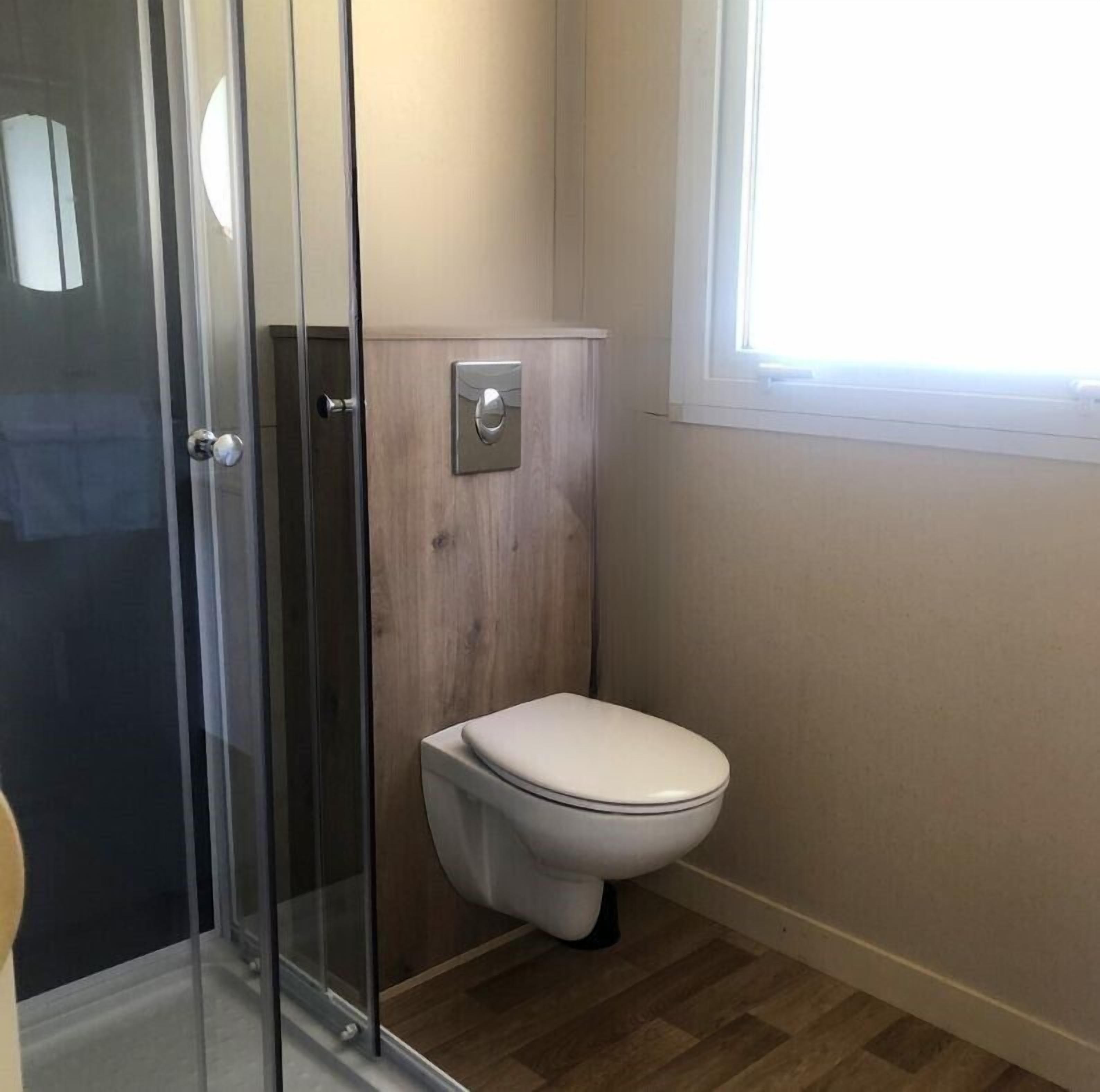 A bathroom with a glass shower enclosure, a toilet, and a window providing natural light.