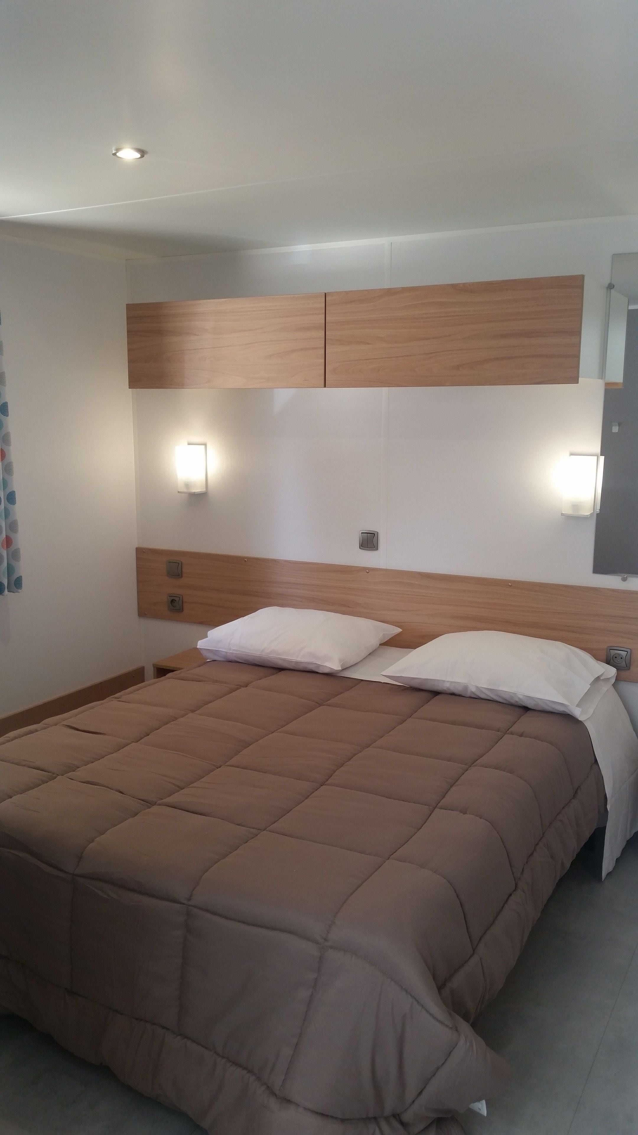 Une chambre à coucher avec un grand lit, une tête de lit en bois, deux tables de chevet et des lampes fixées au mur.