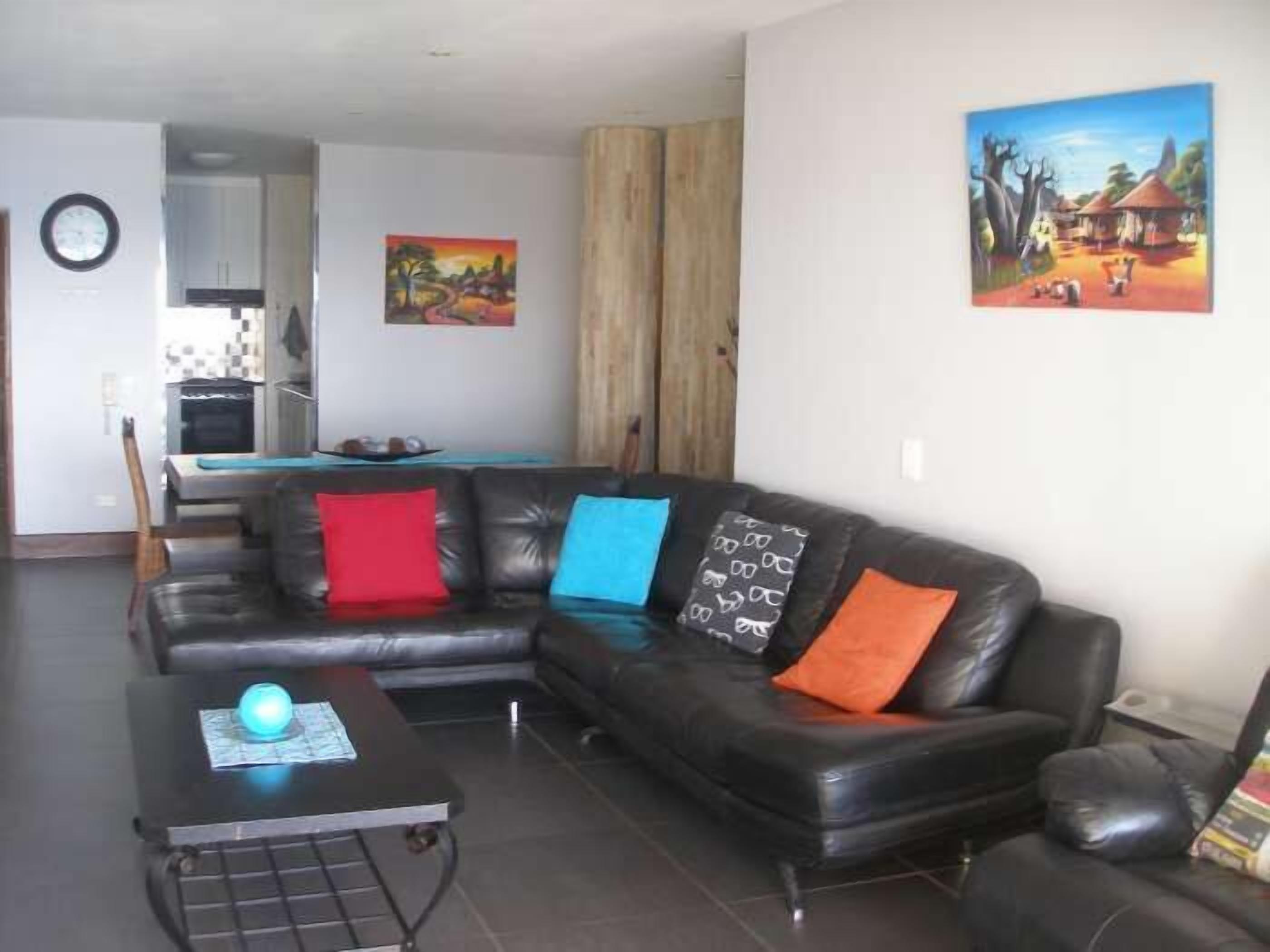 A living room with a black leather sofa, a coffee table with a globe, and two paintings on the wall.
