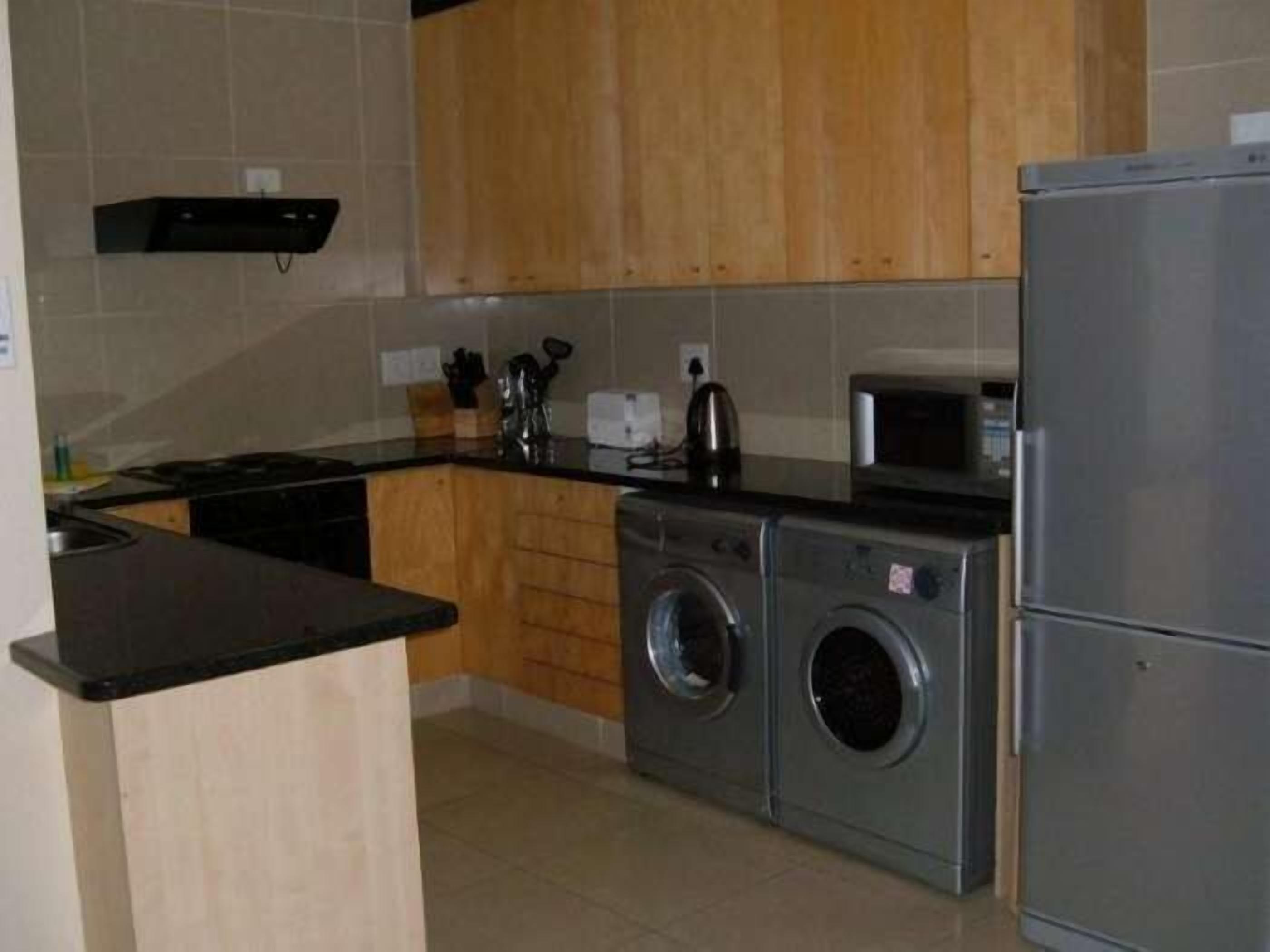 A compact kitchen with wooden cabinets, a built-in washing machine, a microwave, and a sink.