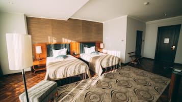Une chambre d’hôtel avec deux lits, une grande moquette à motifs, un banc et une tête de lit en bois.