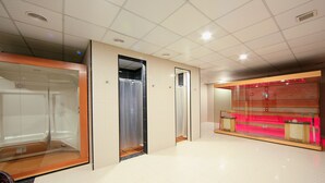 Un vestíbulo de hotel con mostrador de recepción, un ascensor de vidrio y una zona de duchas.
