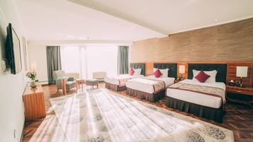 A hotel room with two beds, a large rug, a desk, a chair, and a TV.