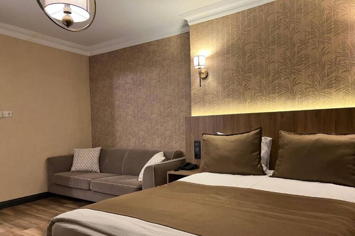 A hotel room with a large bed, a sofa, a nightstand, and a wall-mounted lamp.