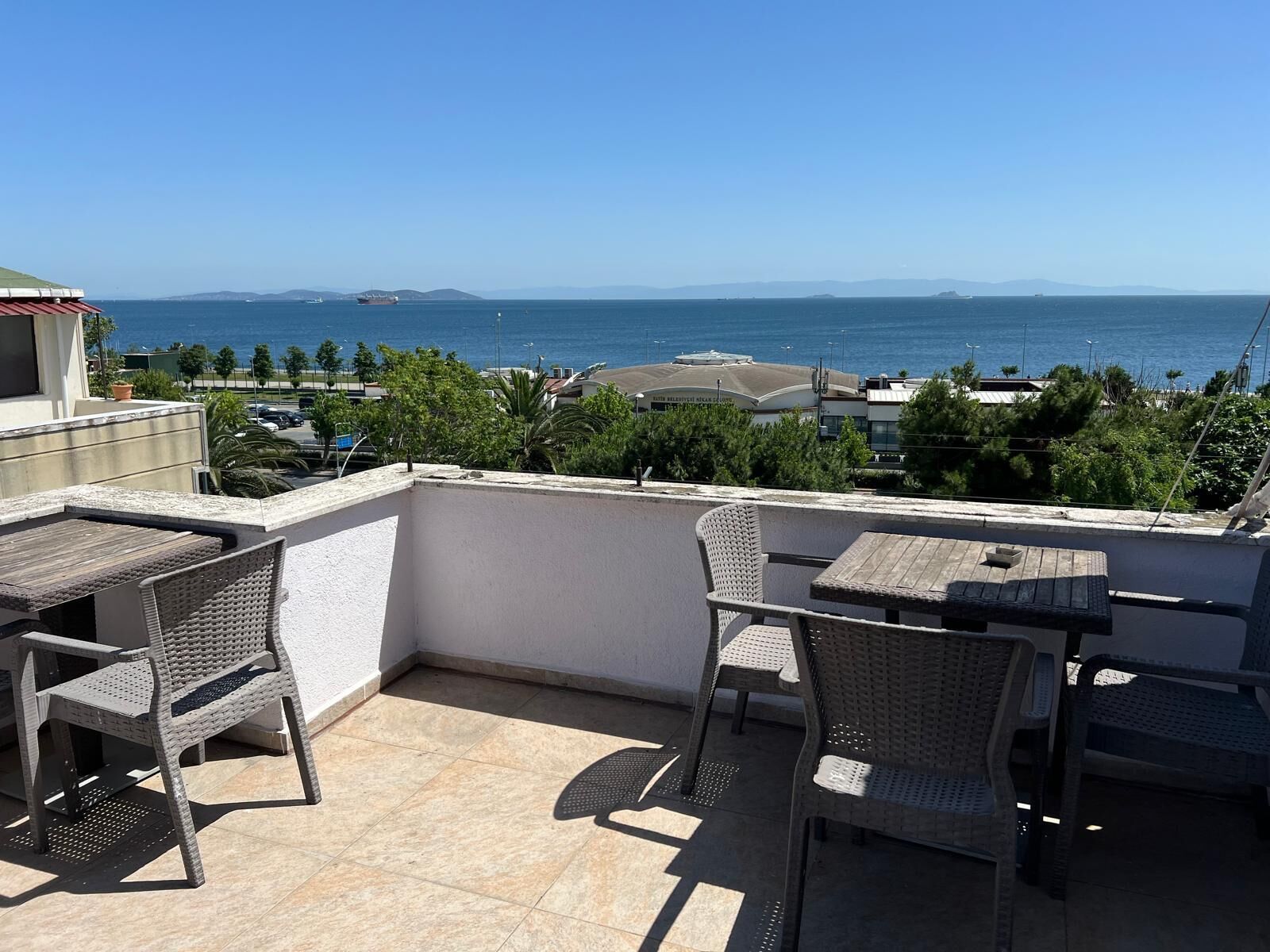 Une terrasse meublée de mobilier en osier, avec vue sur la mer et sur des bâtiments situés au loin.