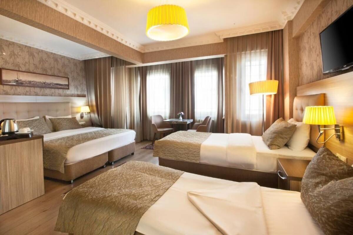A hotel room with two beds, a desk, a chair, a TV, and a large window with curtains.