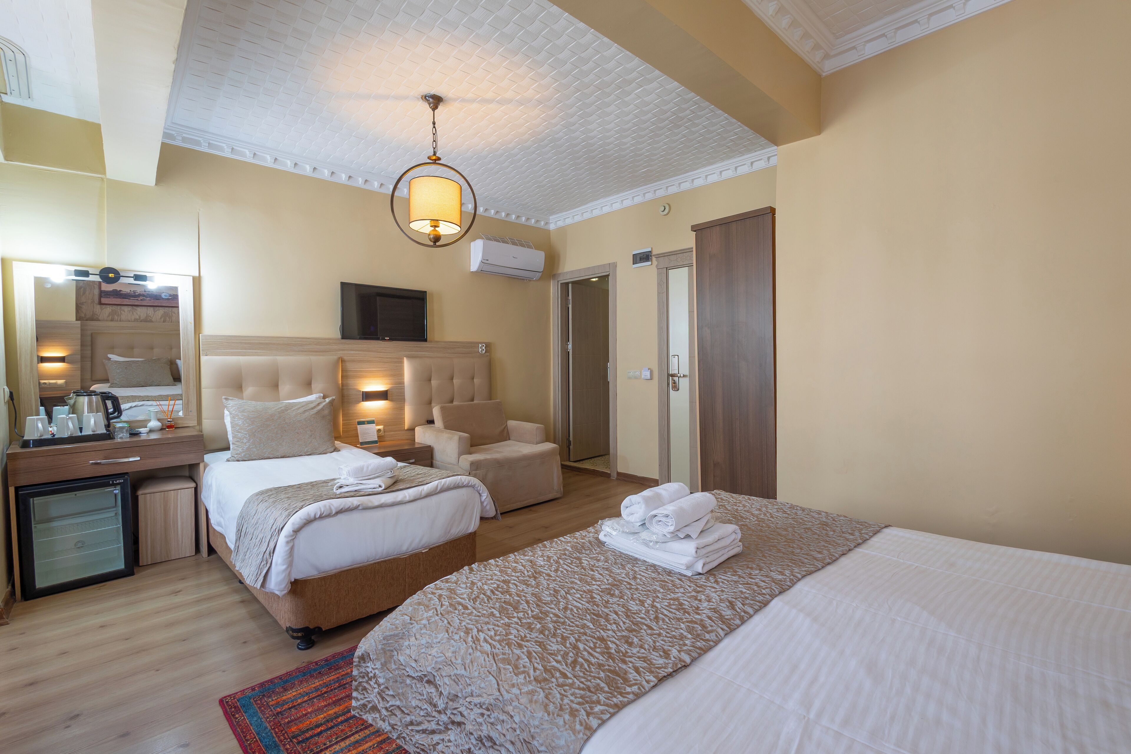 A hotel room with a large bed, a smaller bed, a desk with a lamp, a chair, and a wardrobe.