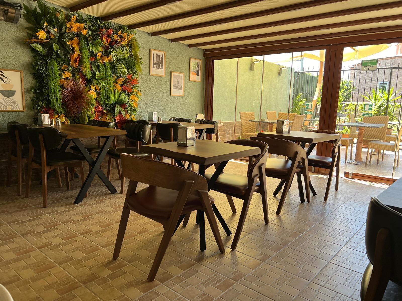 Un restaurant avec des tables et des chaises en bois, un mur végétal agrémenté d’une composition florale et des tableaux encadrés.