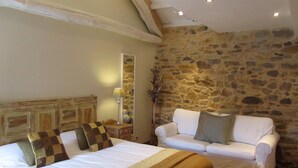 A bedroom with a large bed, a white sofa, a stone wall, and a wooden ceiling.