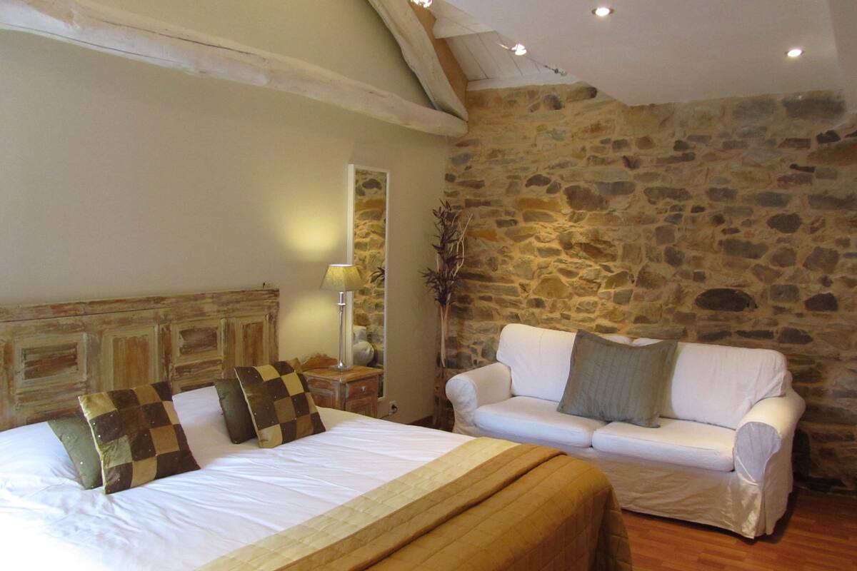 Un dormitorio con una cama grande, un sofá blanco, una pared de piedra y un techo de madera.