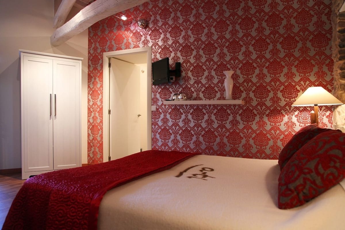 Un dormitorio con una cama, un armario, una puerta, una estantería con adornos y una lámpara.