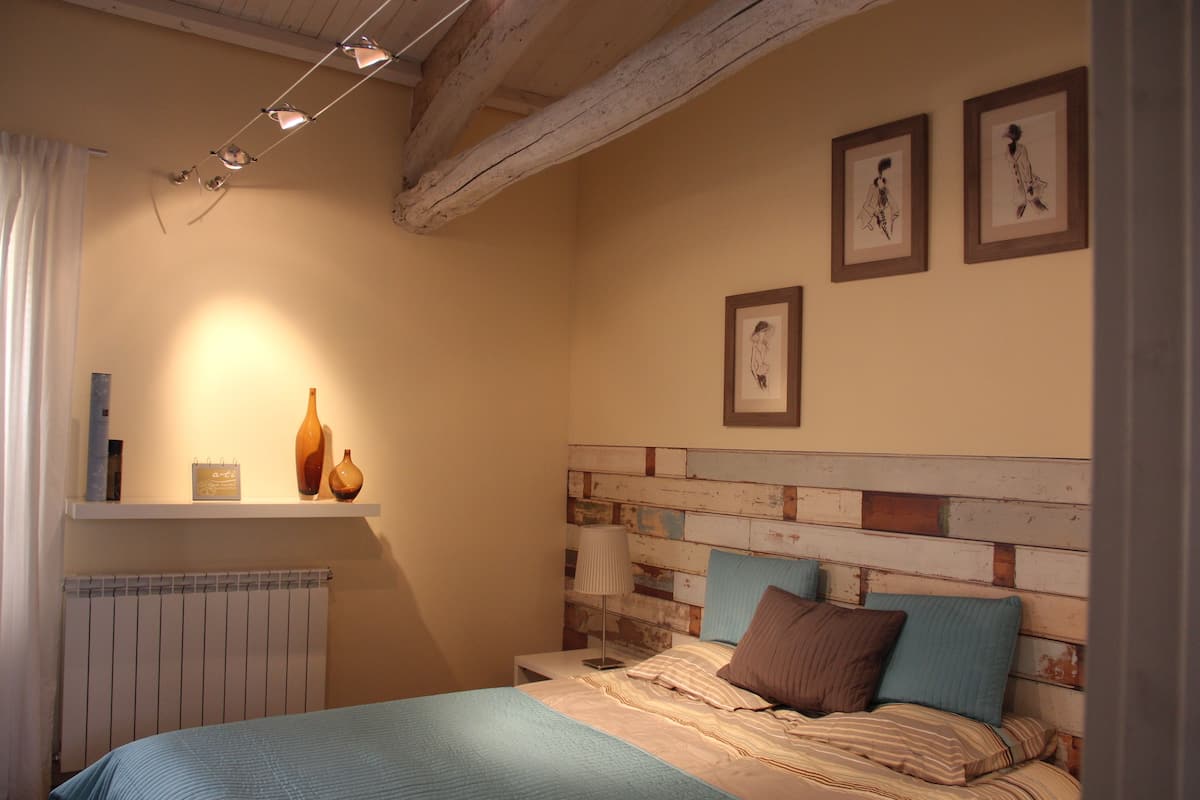 Un dormitorio con cabecera de madera, cama con ropa de cama a rayas, mesita de noche con lámpara y dos cuadros enmarcados en la pared.
