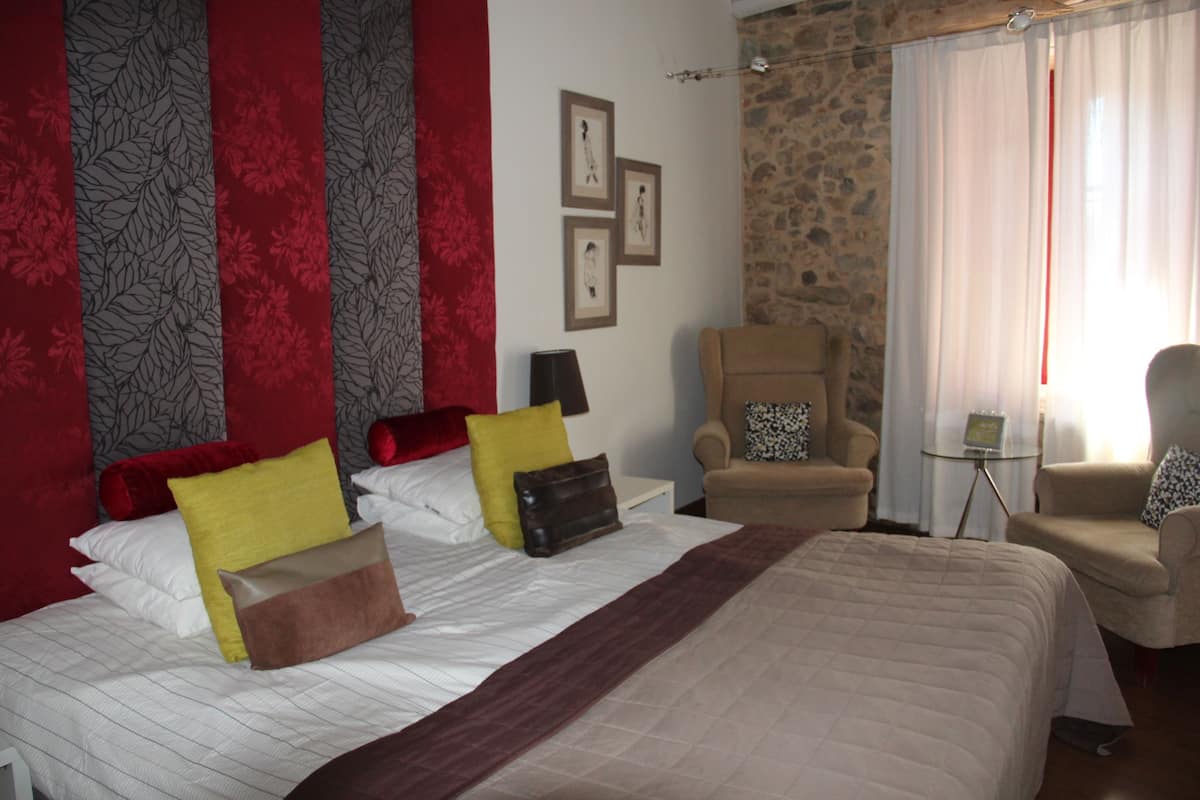 Una habitación de hotel con una cama grande, dos sillones, una mesita y una pared de piedra.