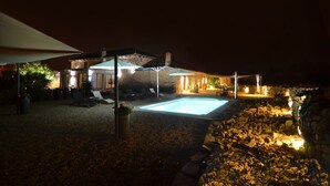A nighttime outdoor area with a swimming pool, lounge chairs, and umbrellas.