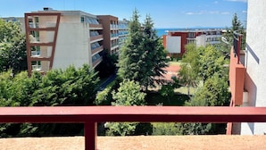 Ein mehrgeschossiges Gebäude mit Balkonen, umgeben von viel Grün und blauem Himmel.