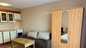 Ein gemütlicher Raum mit Küchenzeile, einer Couch mit Kissen, einem Holzschrank mit Spiegel und einem kleinen Tisch.