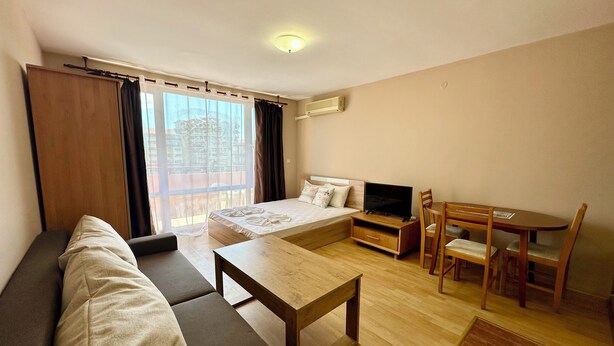 Ein modernes Hotelzimmer mit Sofa, einem kleinen Esstisch, einem Fernseher und einem Balkon mit Vorhängen.