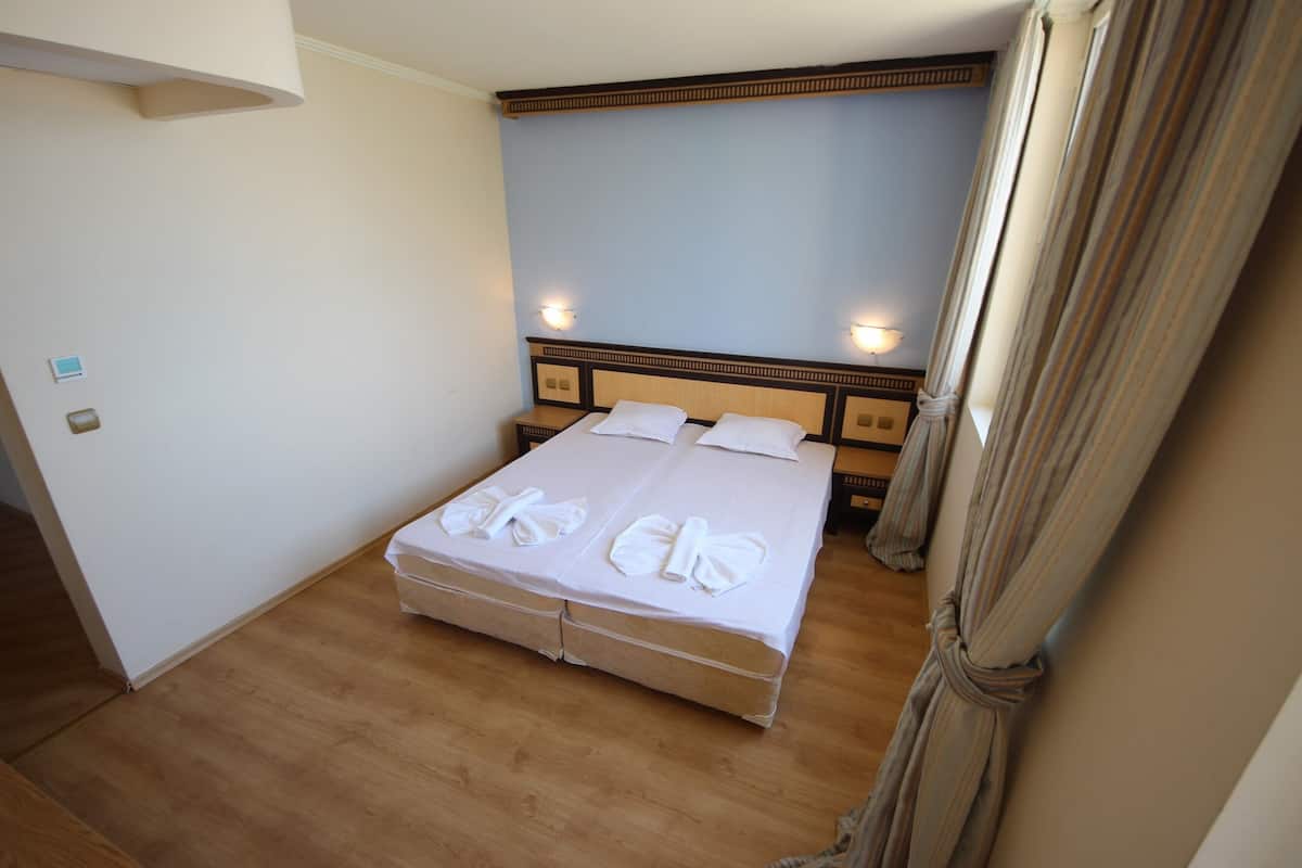 A hotel room with a large bed, wooden headboard, two wall-mounted lights, and a curtain.