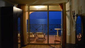 Habitación con vista al mar, balcón con sillas y una mesa, y puerta que da al exterior.