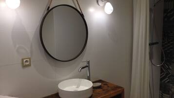 Un baño con un espejo redondo, un lavabo blanco y dos luces fijadas a la pared.