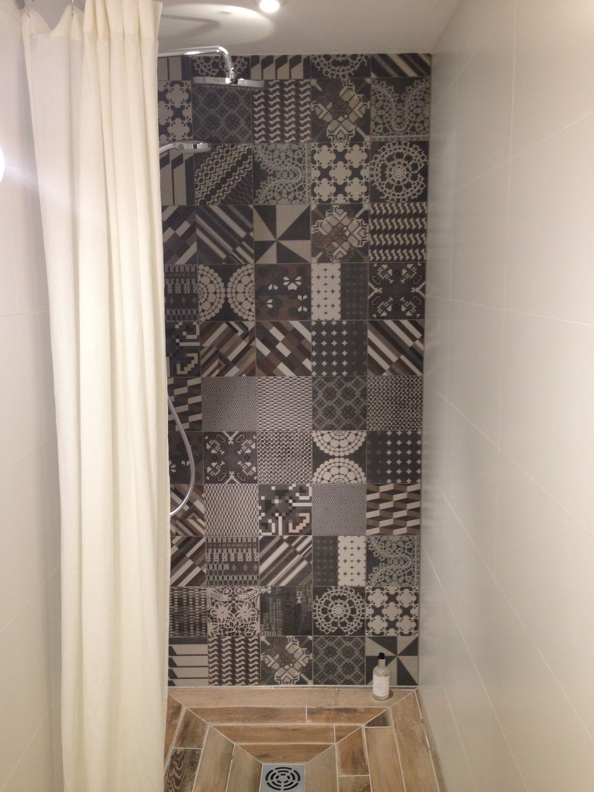 A shower area with a patterned tile wall and a white curtain.