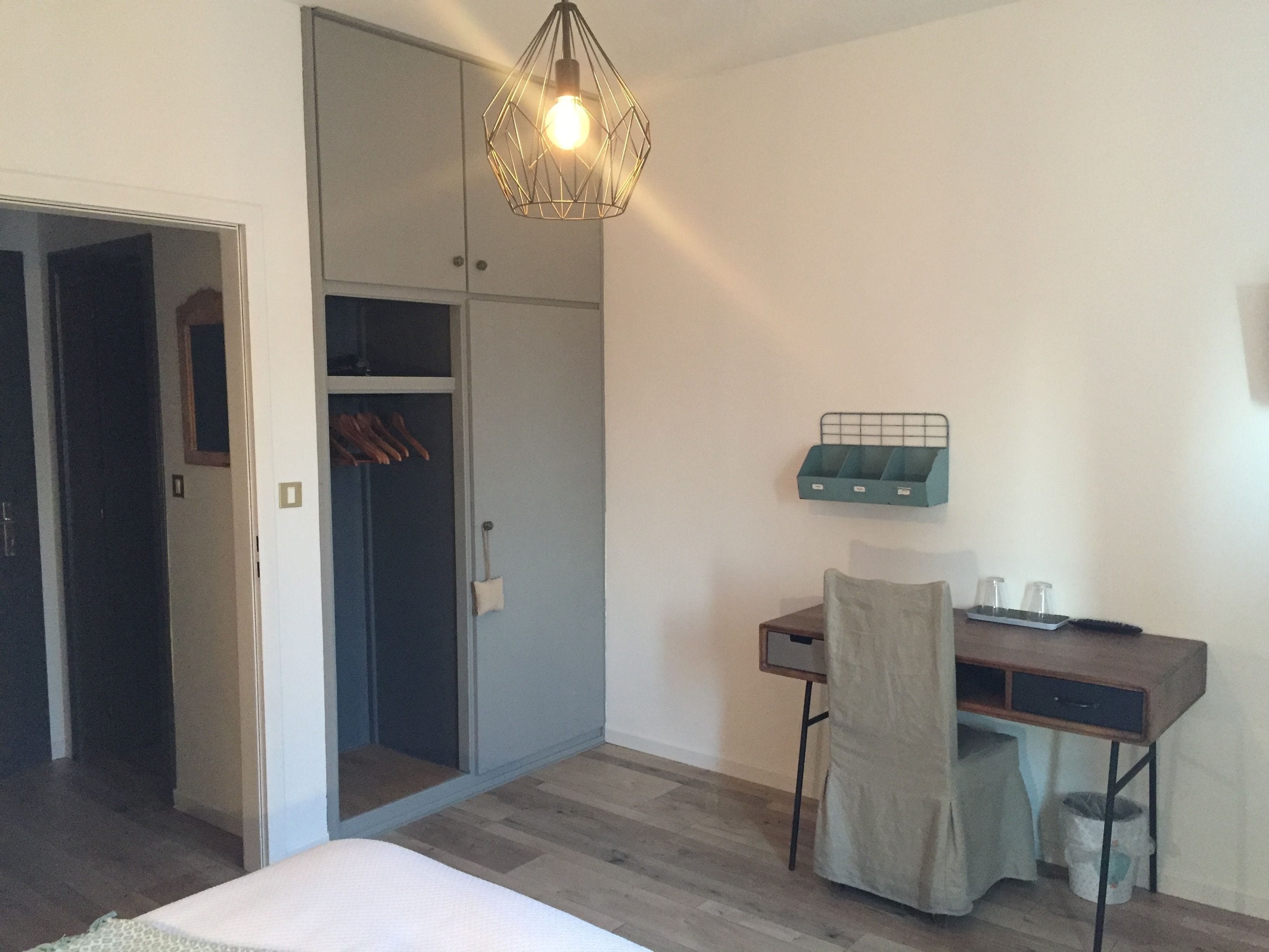 A bedroom with a bed, a desk, a chair, a wardrobe, and a hanging light fixture.