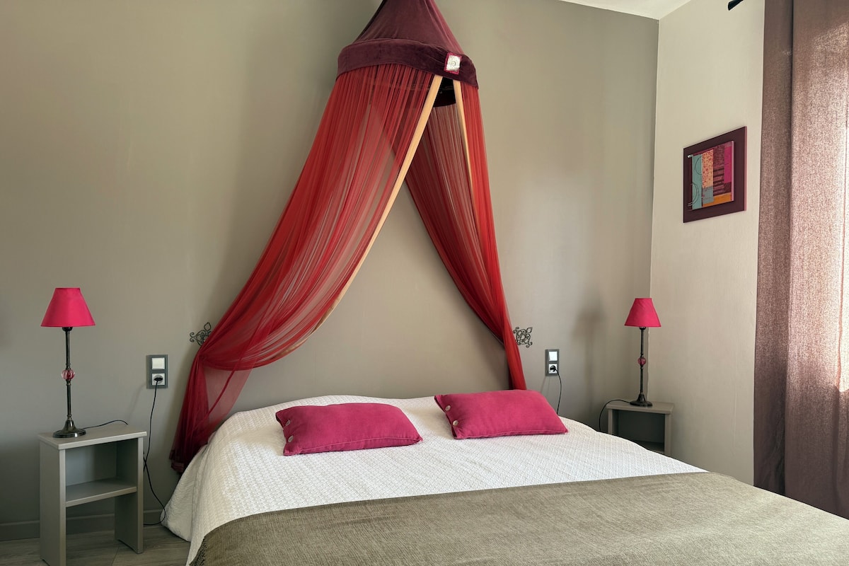 A bedroom with a bed, two bedside tables, a red canopy, and two lamps.